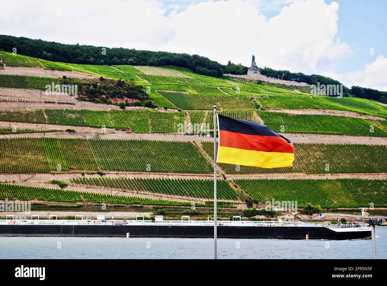 Bingen am Rhein, Allemagne: Rhin avec un bateau, drapeau allemand et vignobles. Niederwalddenkmal, statue de Germania, monument de la réunification allemande. Banque D'Images