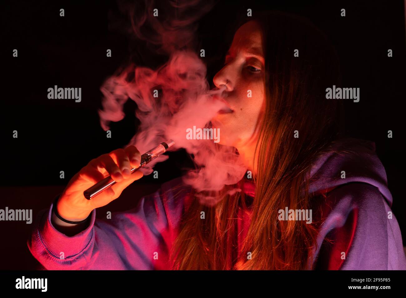 Vaping concept Lifestyle.Jeune fille fume avec des lumières de couleur néon dans le studio d'arrière-plan sombre. Banque D'Images