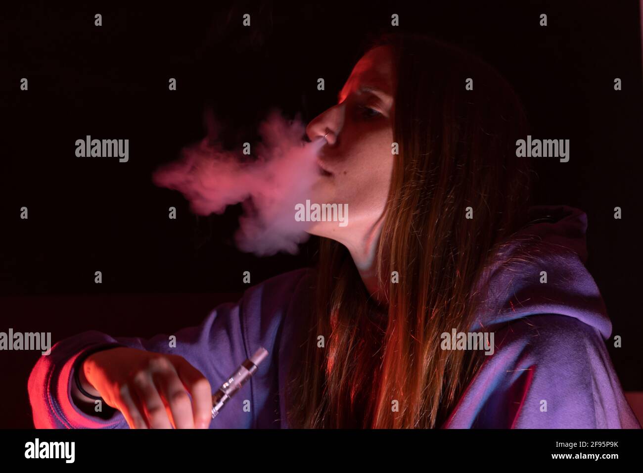 Jeune femme vapoing avec des lumières de couleur.Closeup Smoke concept, style de vie caucasien couche fille avec espace de copie. Banque D'Images