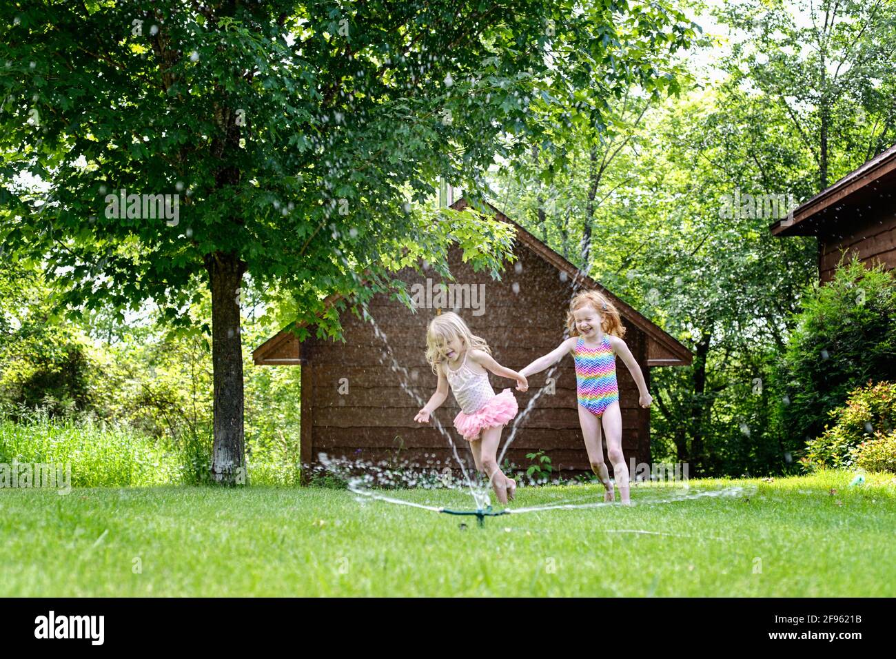 Deux jolies petites filles jouant à l'extérieur dans un arroseur à eau. Banque D'Images