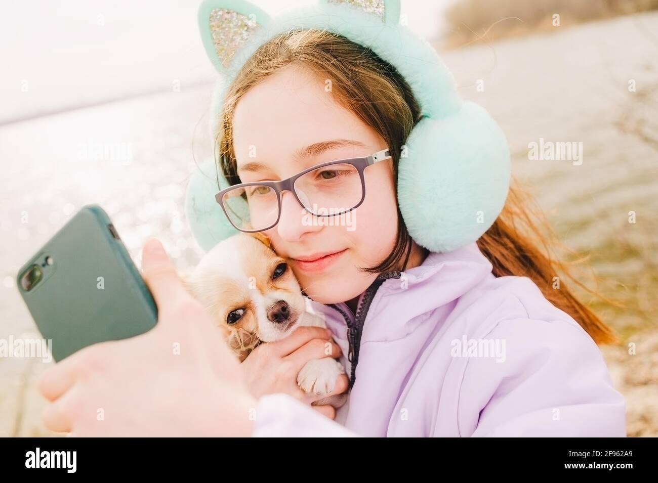 Fille fait selfie sur smartphone. Portrait d'une jeune fille heureuse avec son petit chien chihuahua. Une fille sur le fond de la nature embrasse son chien Chihuahua en vêtements. Banque D'Images
