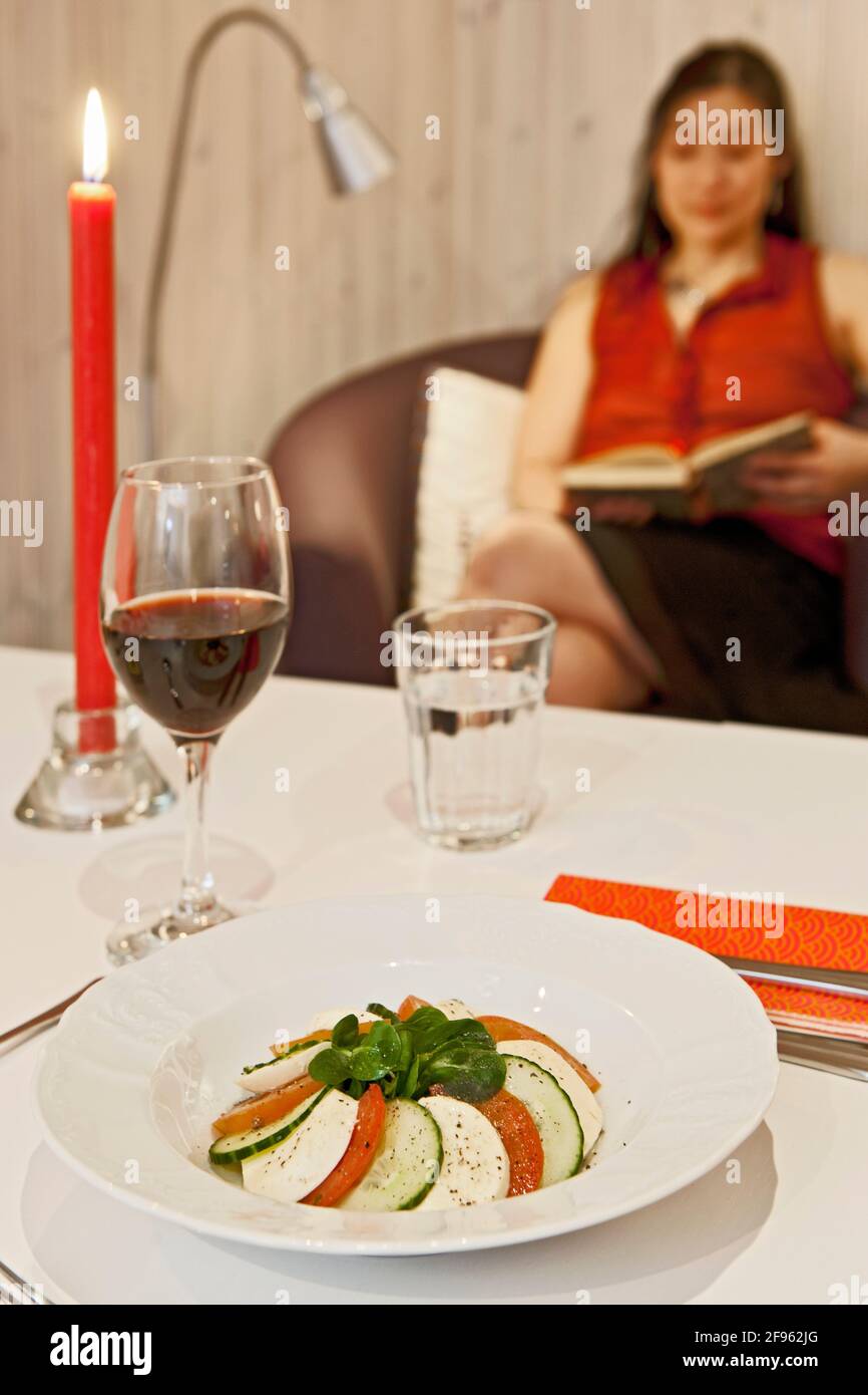 salade caprese sur table avec une femme lisant en arrière-plan Banque D'Images