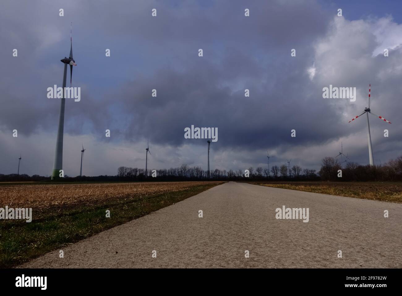éoliennes champs sombres nuages et une longue rue avec neige Banque D'Images