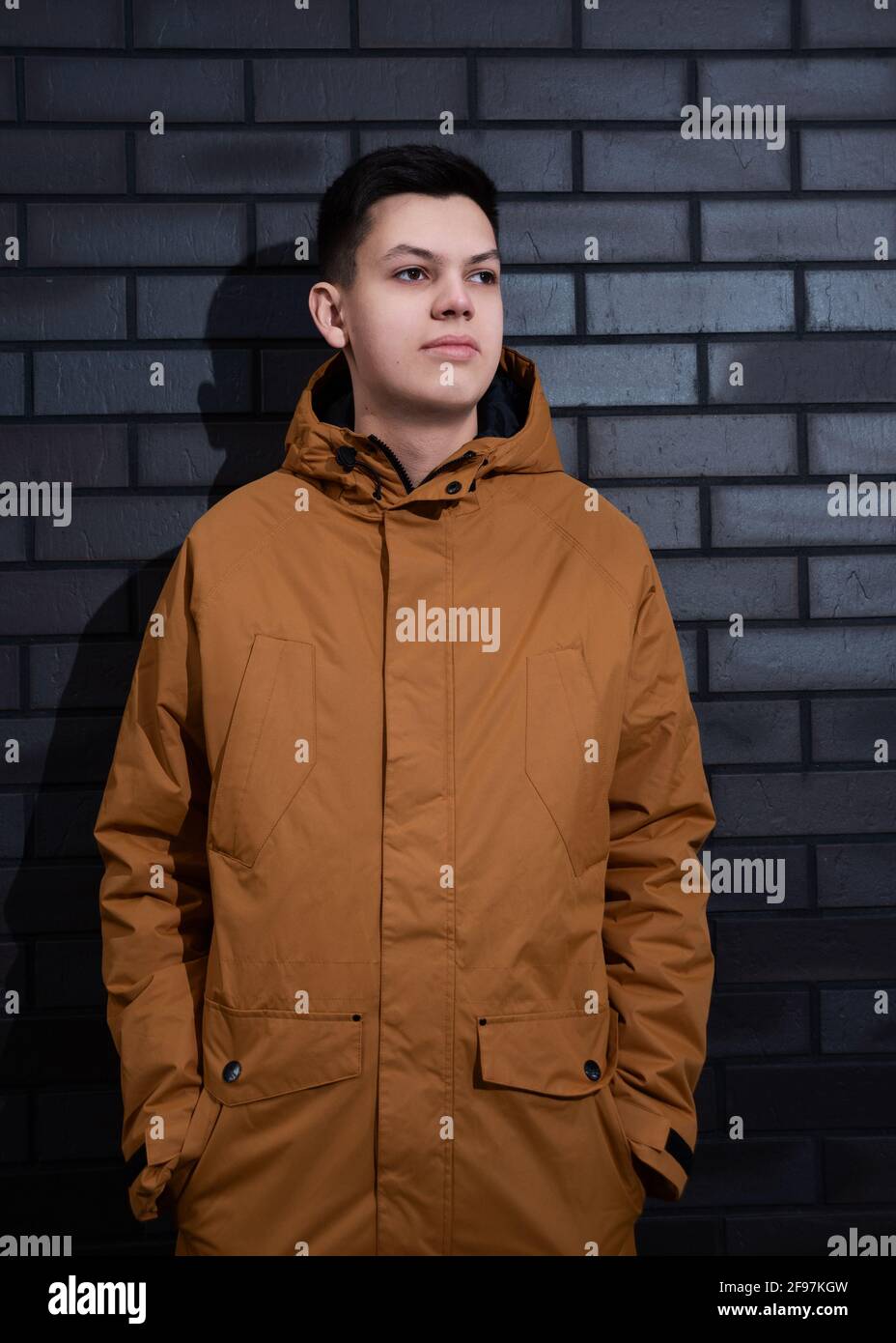 Beau garçon adolescent posant contre le mur de briques brun foncé à  l'extérieur. Portrait d'un jeune homme du caucase vêtu d'une veste jaune de  couleur moutarde Photo Stock - Alamy