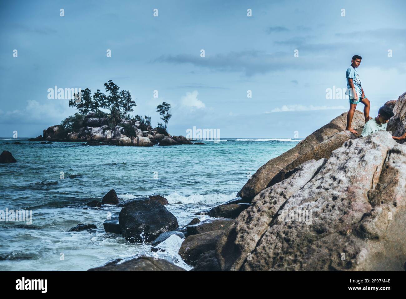 Un jeune homme debout sur un rocher aux Seychelles: L'eau turqoise cristalline, le sable blanc, les palmiers - tout ressemble à un rêve Banque D'Images