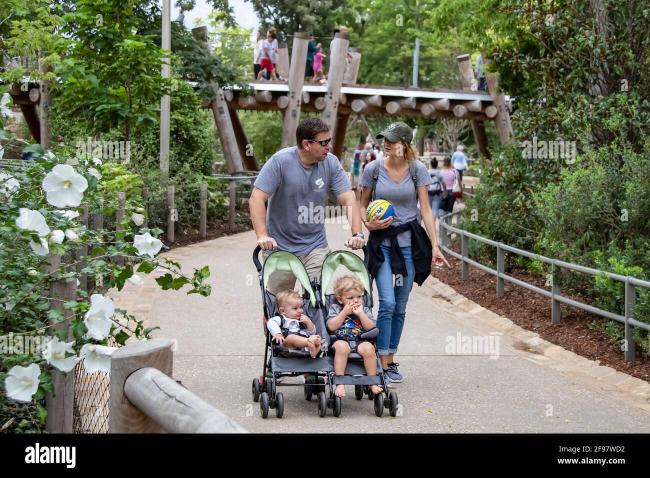 Tulsa États-Unis 9-8-2018 les parents marchent le long de la voie poussant 2 bébés dans un double chariot parlant l'un à l'autre pendant qu'elle porte un ballon de basket-ball avec pont Banque D'Images