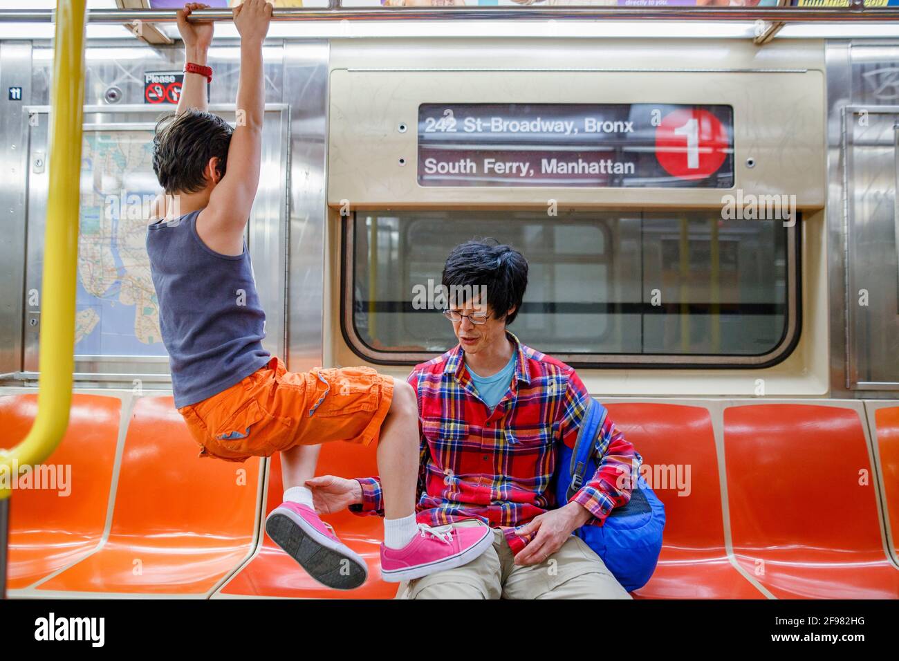 Un petit garçon est suspendu à la main courante dans le métro de New York  et son père le tire vers le bas Photo Stock - Alamy