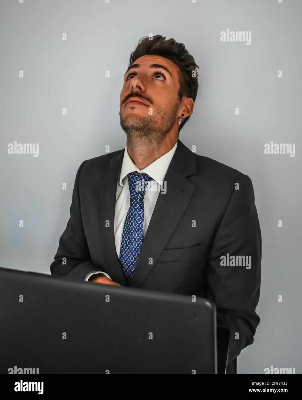 Homme d'affaires espagnol dans un costume regardant vers le haut en face d'un ordinateur portable Banque D'Images