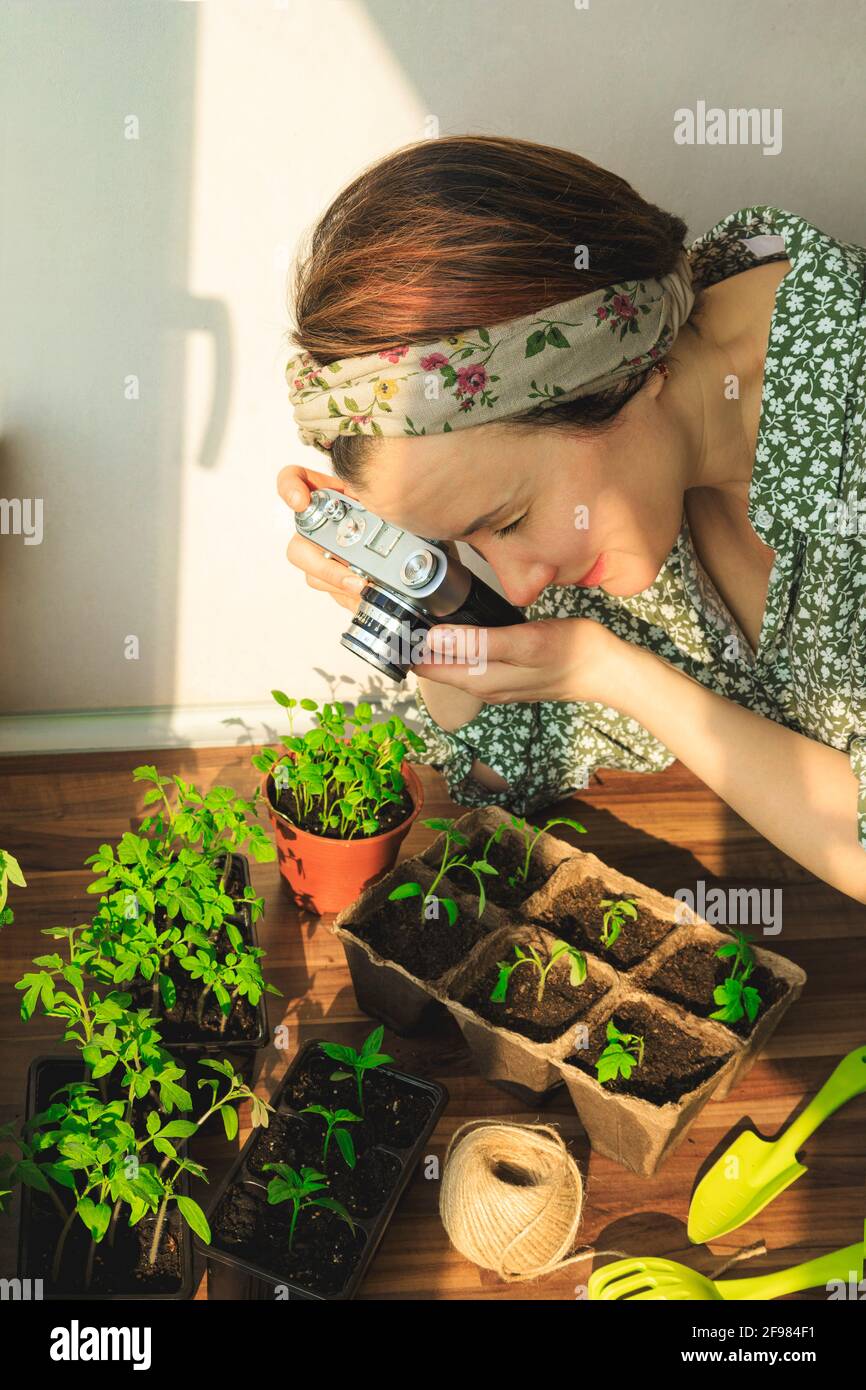 Une femme prend des photos avec un appareil photo rétro des plantes qu'elle a grandi dans son jardin à la maison pour son blog. Banque D'Images
