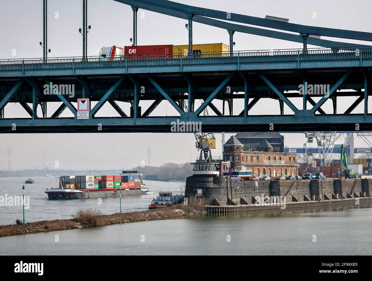 Krefeld, Rhénanie-du-Nord-Westphalie, Allemagne - le Rheinhafen Krefeld est le quatrième plus grand port de la Rhénanie-du-Nord-Westphalie, un bateau à conteneurs passe devant le terminal KCT Krefelder, devant un camion conduit sur le pont Krefeld-Uerdinger au-dessus du Rhin. Banque D'Images