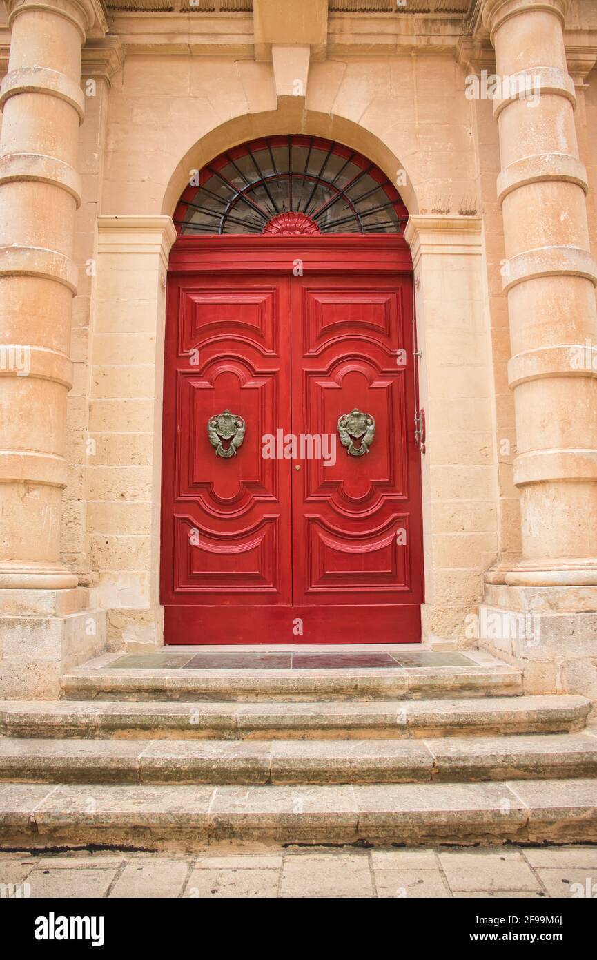 Marches menant à une porte rouge vibrante et des knockers de porte ornés sur un bâtiment à Mdina, Malte. Banque D'Images