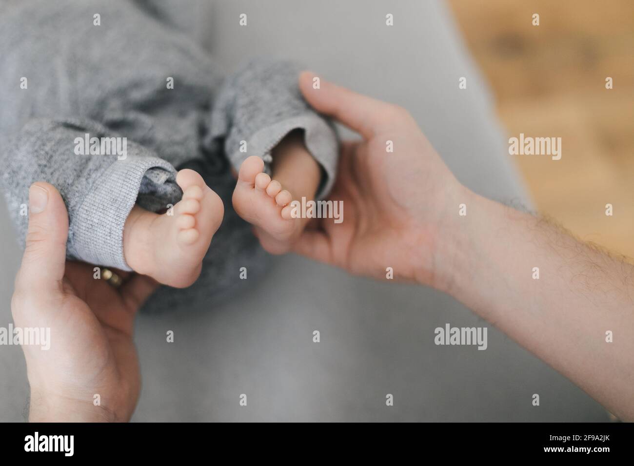 Photo d'une jeune mère ou d'un médecin mains tenant les pieds nus du nouveau-né sur fond gris. Joyeux moment de parentalité. Gros plan. Banque D'Images