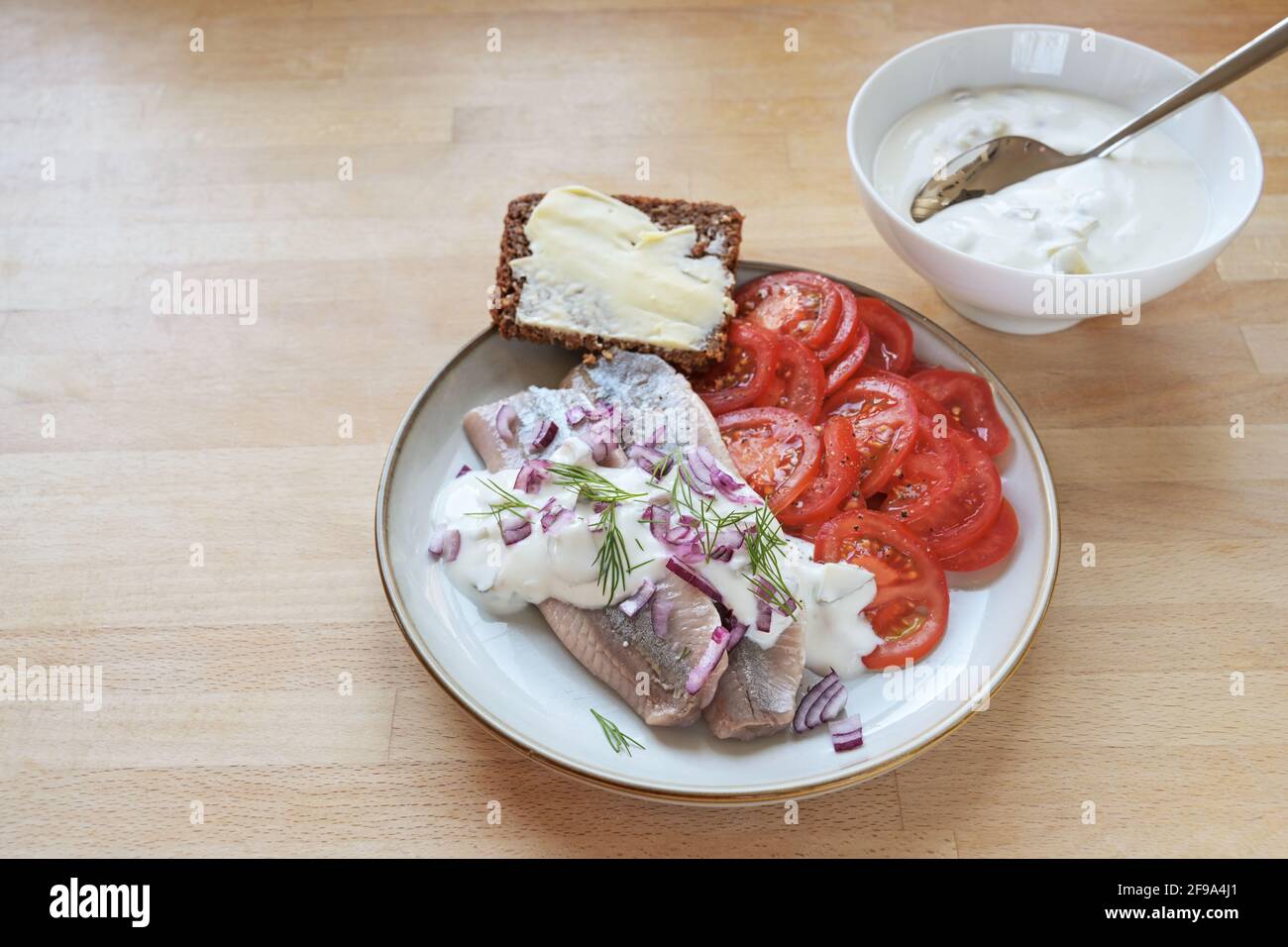 Filets de hareng salés avec sauce à la crème aigre, oignons rouges et aneth sur une assiette avec tranches de tomate et pain de grainl entier foncé, table en bois avec copie sp Banque D'Images