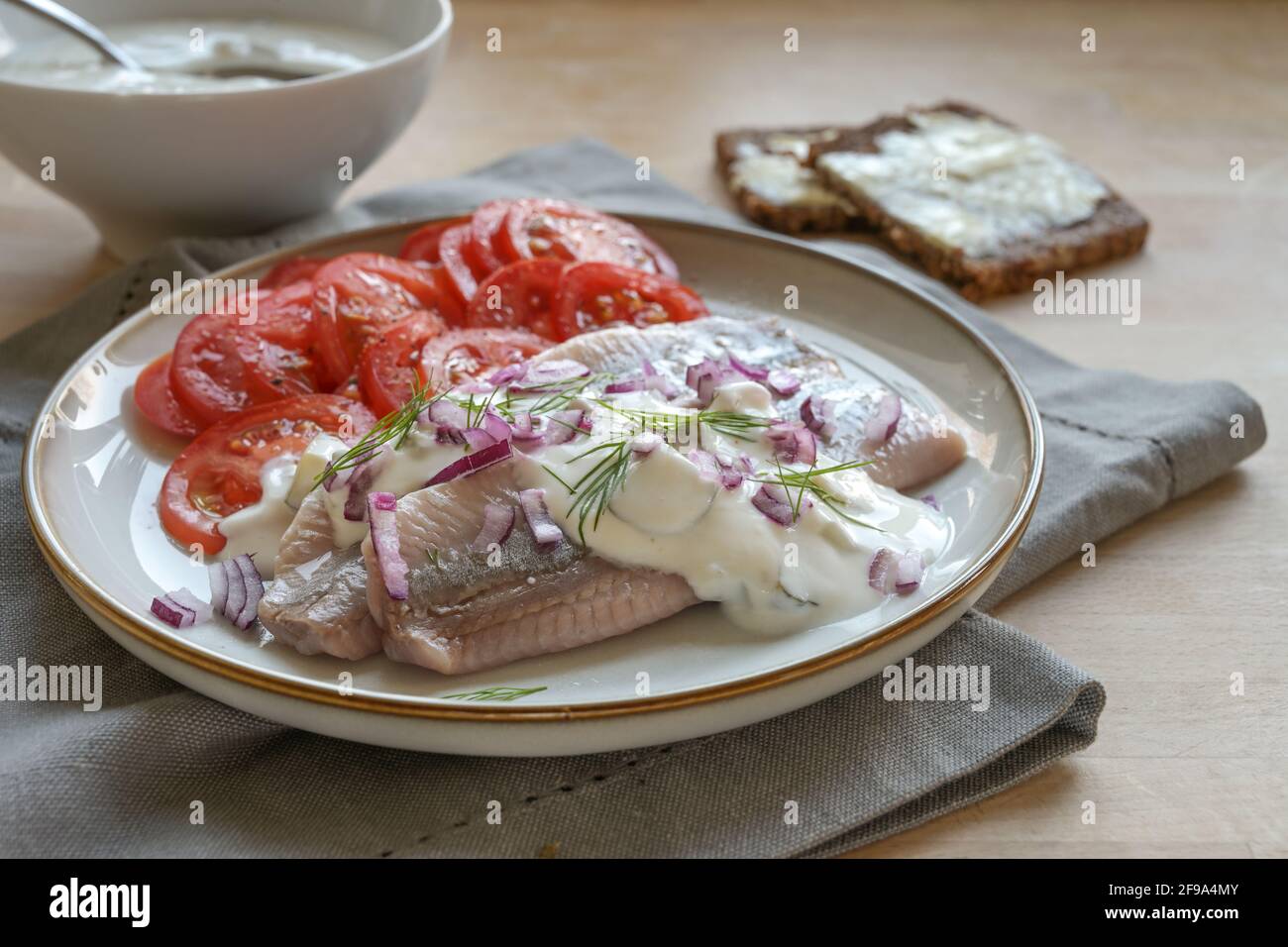 Filets de hareng salé traditionnel hollandais également appelé maatje avec sauce à la crème, oignons rouges, garniture d'aneth et salade de tomates servis sur une assiette sur un bois Banque D'Images