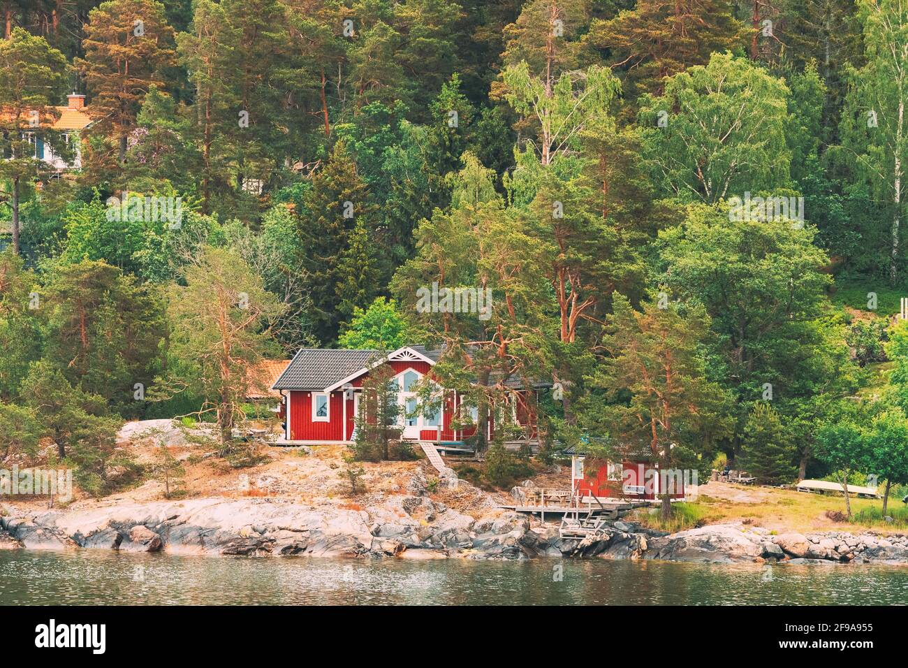 Suède. Magnifiques chalets en bois rouge ASwedish Maisons sur la côte des Rocheuses en été. Paysage de lac ou de rivière Banque D'Images