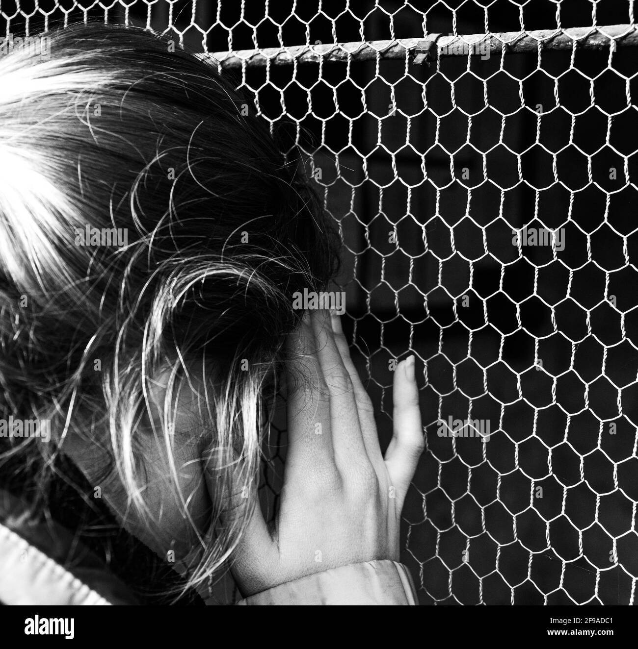 Photo en niveaux de gris d'une jeune femme regardant à travers un métal clôture Banque D'Images