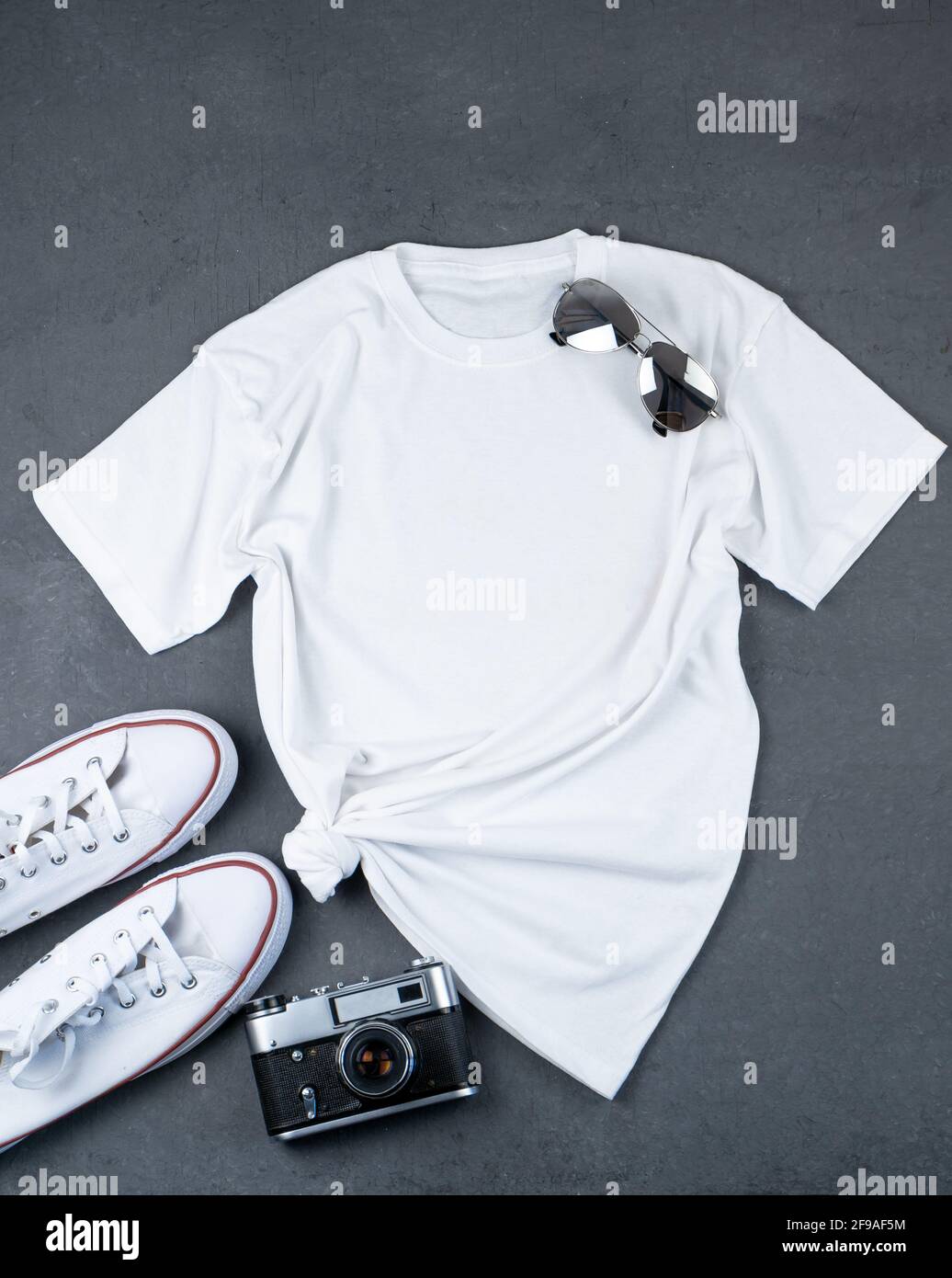 T-shirt blanc avec emplacement pour le texte. Baskets, lunettes, appareil photo - un ensemble de vêtements pour la marche. Maquette de T-shirt pour l'impression. Kit élégant. Arrière-plan gris Banque D'Images