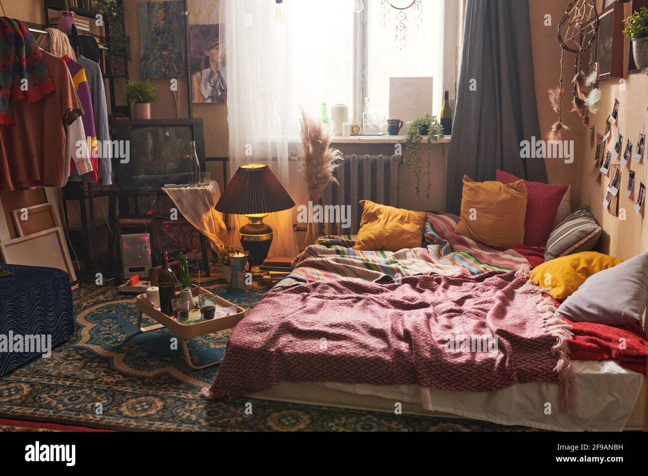 Intérieur d'une chambre à l'ancienne avec des vêtements sur le porte-vêtements et plateau avec une bouteille de vin rouge sur le sol Banque D'Images
