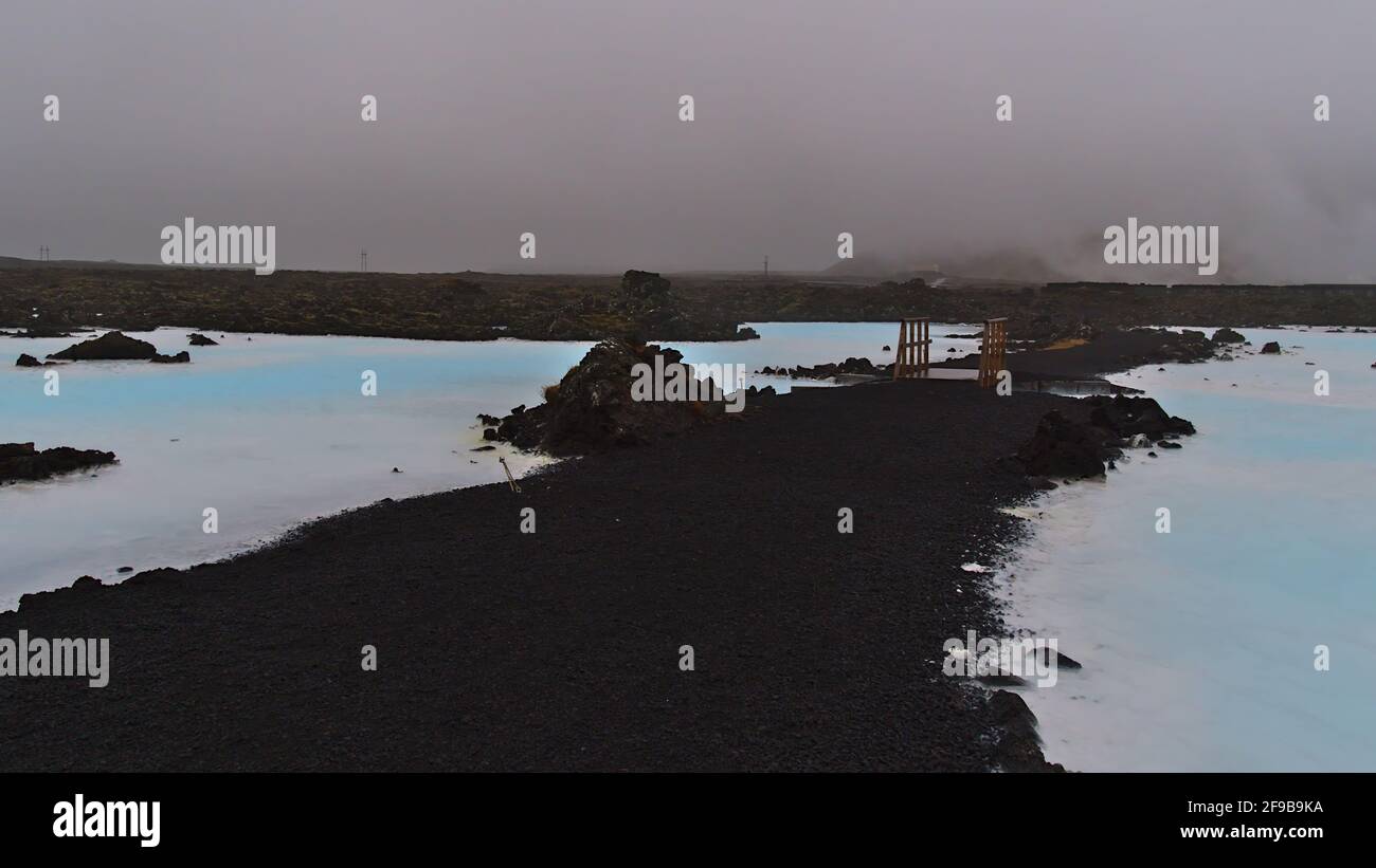 Vue sur une passerelle en bois traversant des piscines d'eau bleue scintillante dans un champ de lave près de la station thermale géothermique Blue Lagoon, Grindavik, Reyjanes, Islande. Banque D'Images