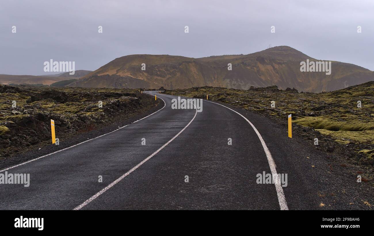 Perspective décroissante de la route sinueuse de pays avec des marques entre les champs de lave couverts de mousse de pierres volcaniques près de Grindavik, Reykjanes, Islande. Banque D'Images