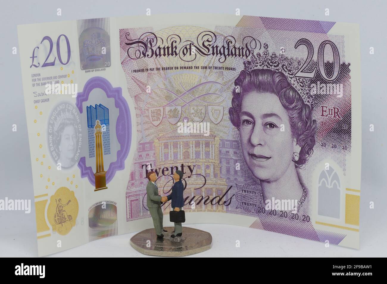 Les hommes d'affaires miniatures se secouent la main devant un billet de 20 GBP. Banque D'Images