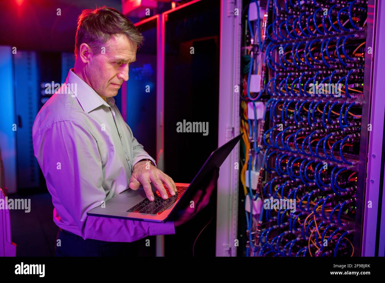 Ingénieur INFORMATIQUE fiable et mature, avec un PC portable à armoire de serveur et utilisation du serveur sous lumière de néon Banque D'Images