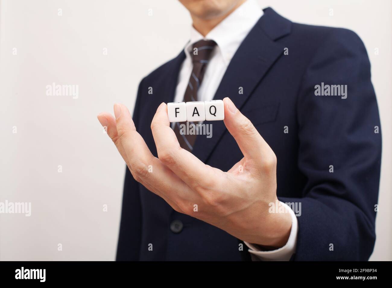 Un cube blanc avec la FAQ écrite dans la main d'une personne d'affaires Banque D'Images