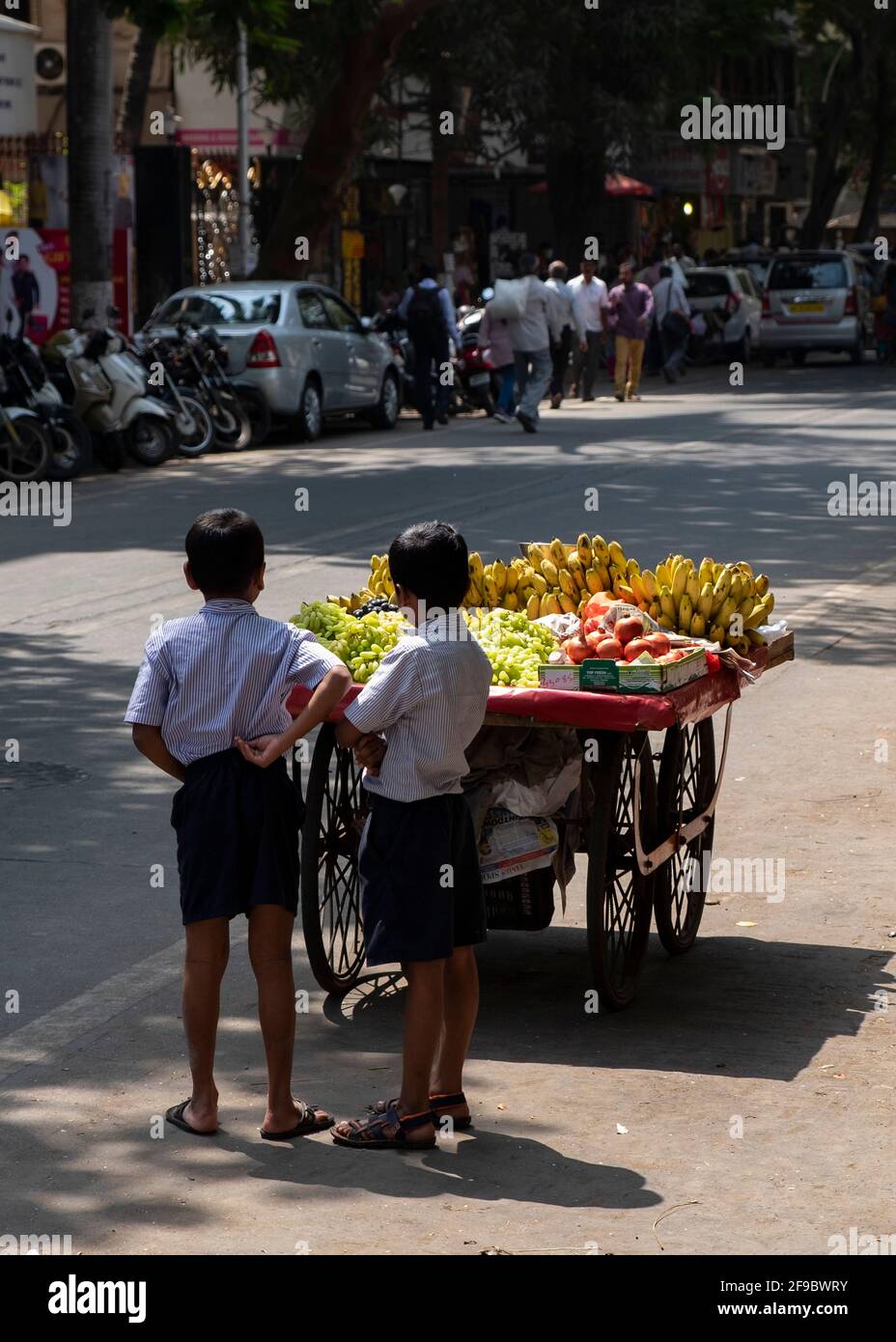 Deux garçons d'école se tenant près d'un chariot de vendeurs de fruits attendant le vendeur dans la banlieue de Mumbai de Dadar, Maharashtra, Inde, Asie. Banque D'Images