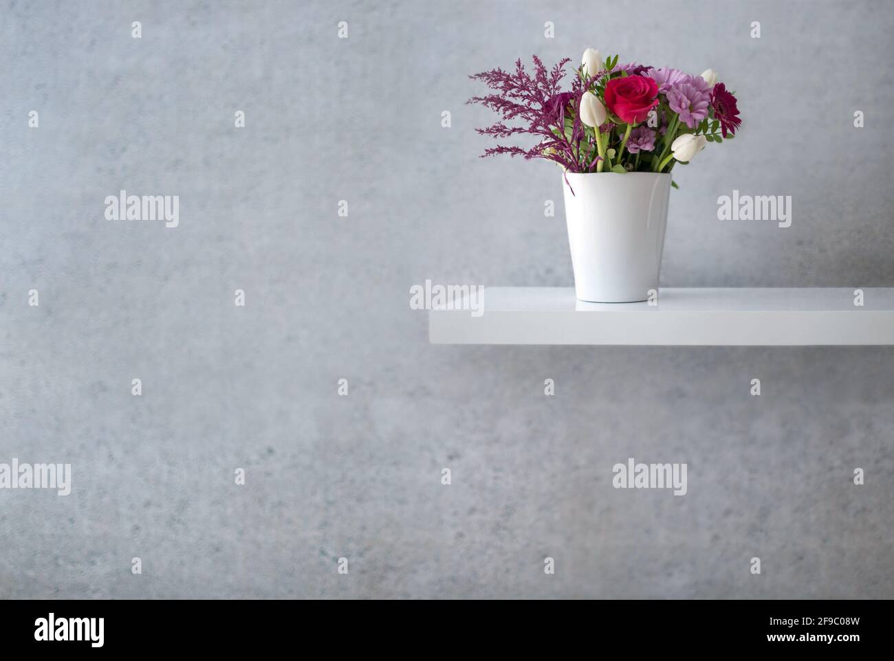Motif fleuri assorti sur une étagère blanche flottante contre un mur en béton Banque D'Images