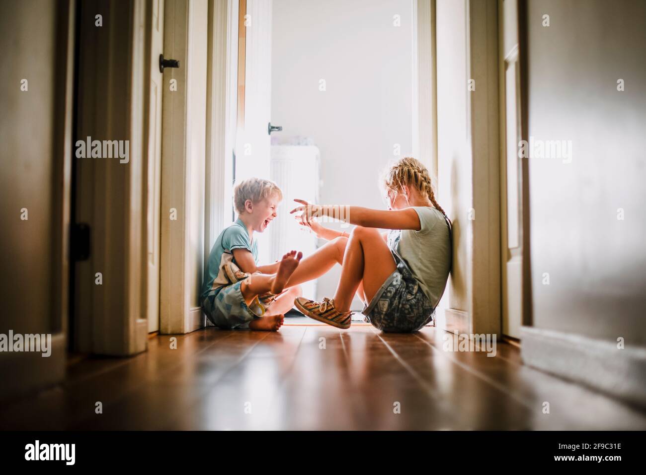 Frère et sœur jouant et riant dans un couloir lumineux Banque D'Images