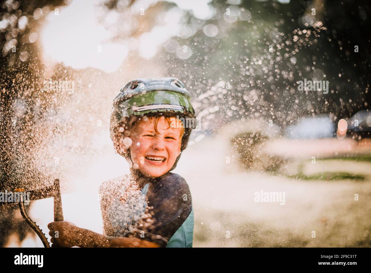 Jeune garçon jouant à l'extérieur dans l'eau d'arrosage éclaboussant et riant Banque D'Images