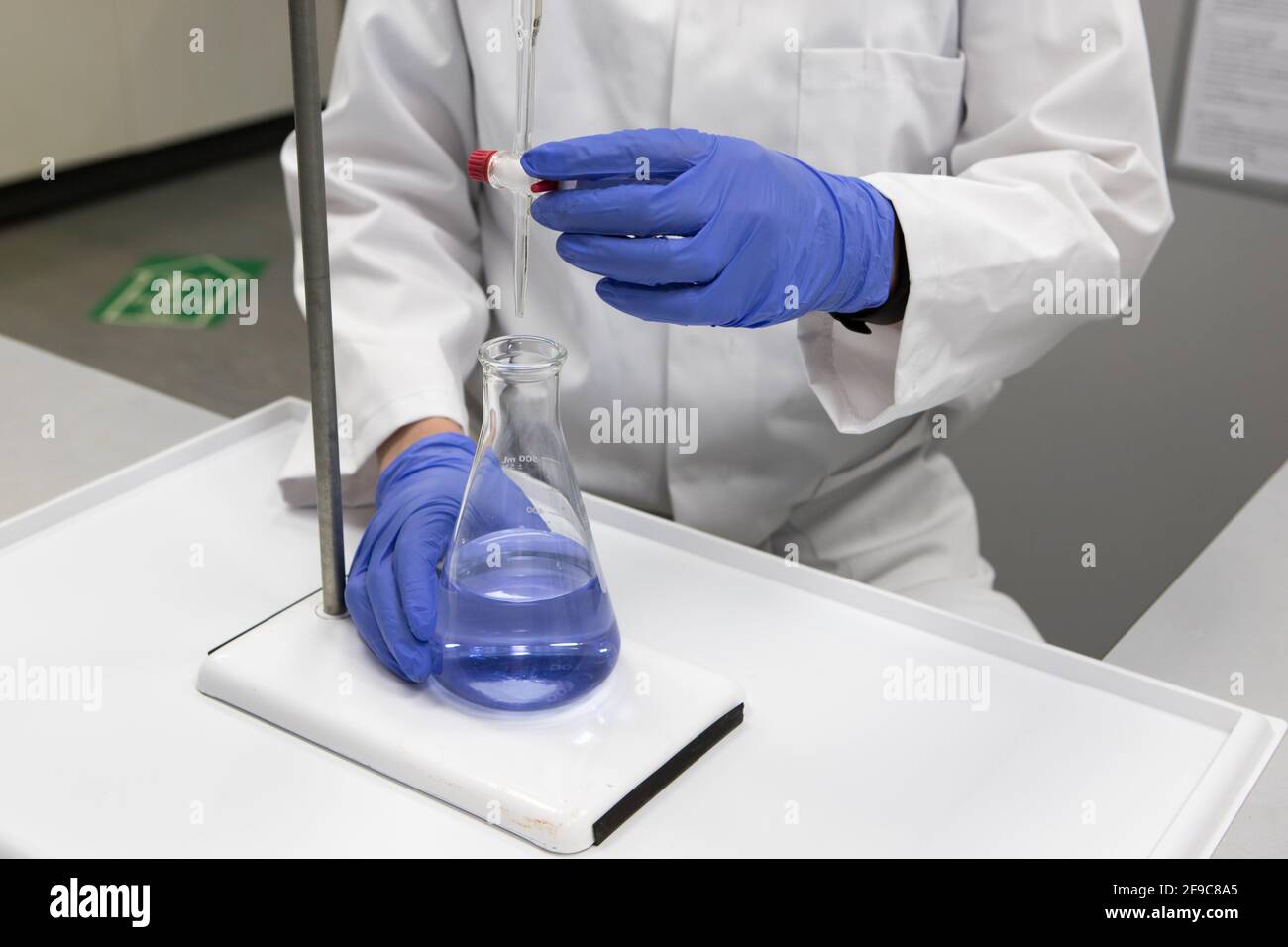 Pharmacien aux mains gantées et blouse de laboratoire blanche analysant un échantillon par titrage Banque D'Images