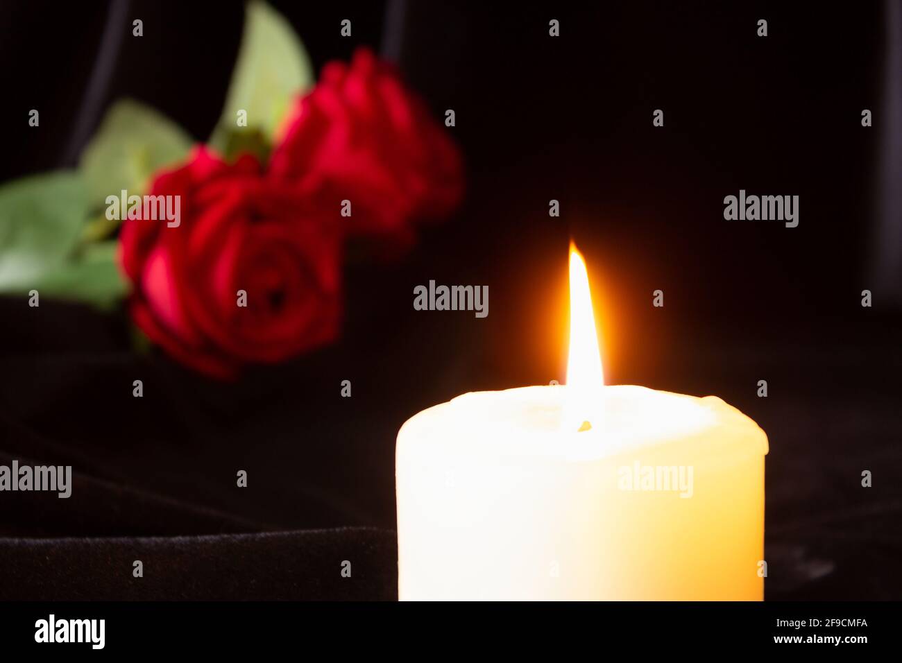 Une bougie allumée et une rose rouge sur fond noir. Le concept de condoléances, de deuil et de funérailles. Banque D'Images