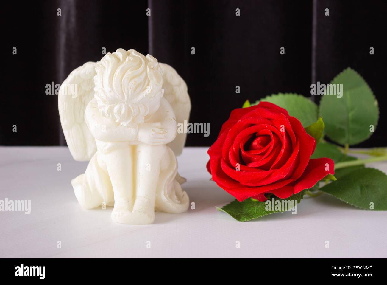 Une Petite Sculpture D Un Ange De Bebe Avec Des Ailes Et Une Rose Rouge Sur Fond Noir Le Concept Des Funerailles Des Condoleances Et Du Deuil Photo Stock Alamy