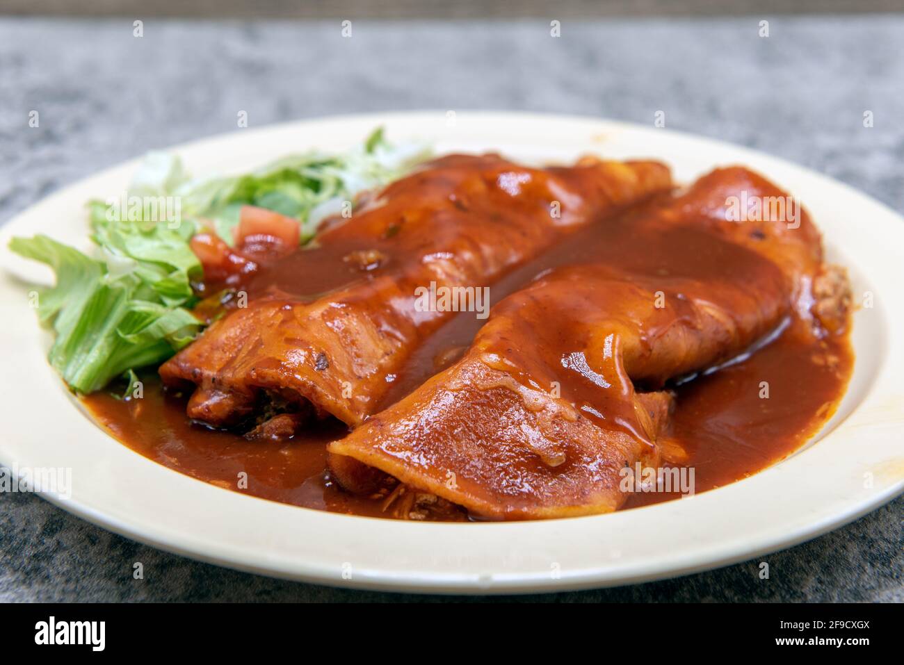 Enchiladas de poulet étouffé dans une sauce rouge savoureuse sur une assiette pour une entrée copieuse et de remplissage. Banque D'Images