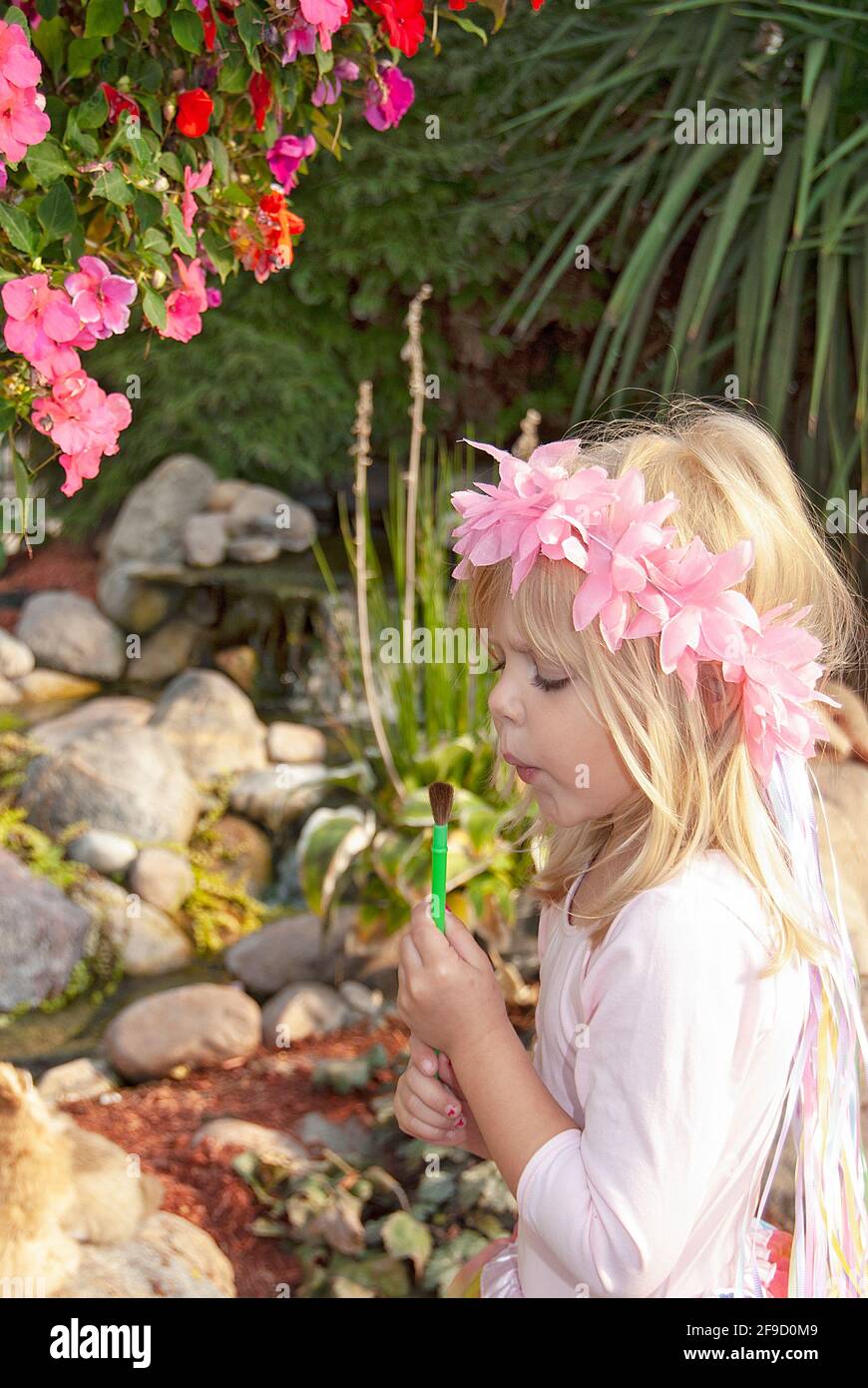 Petite fille blonde de fée soufflant sur pinceau dans le jardin Banque D'Images