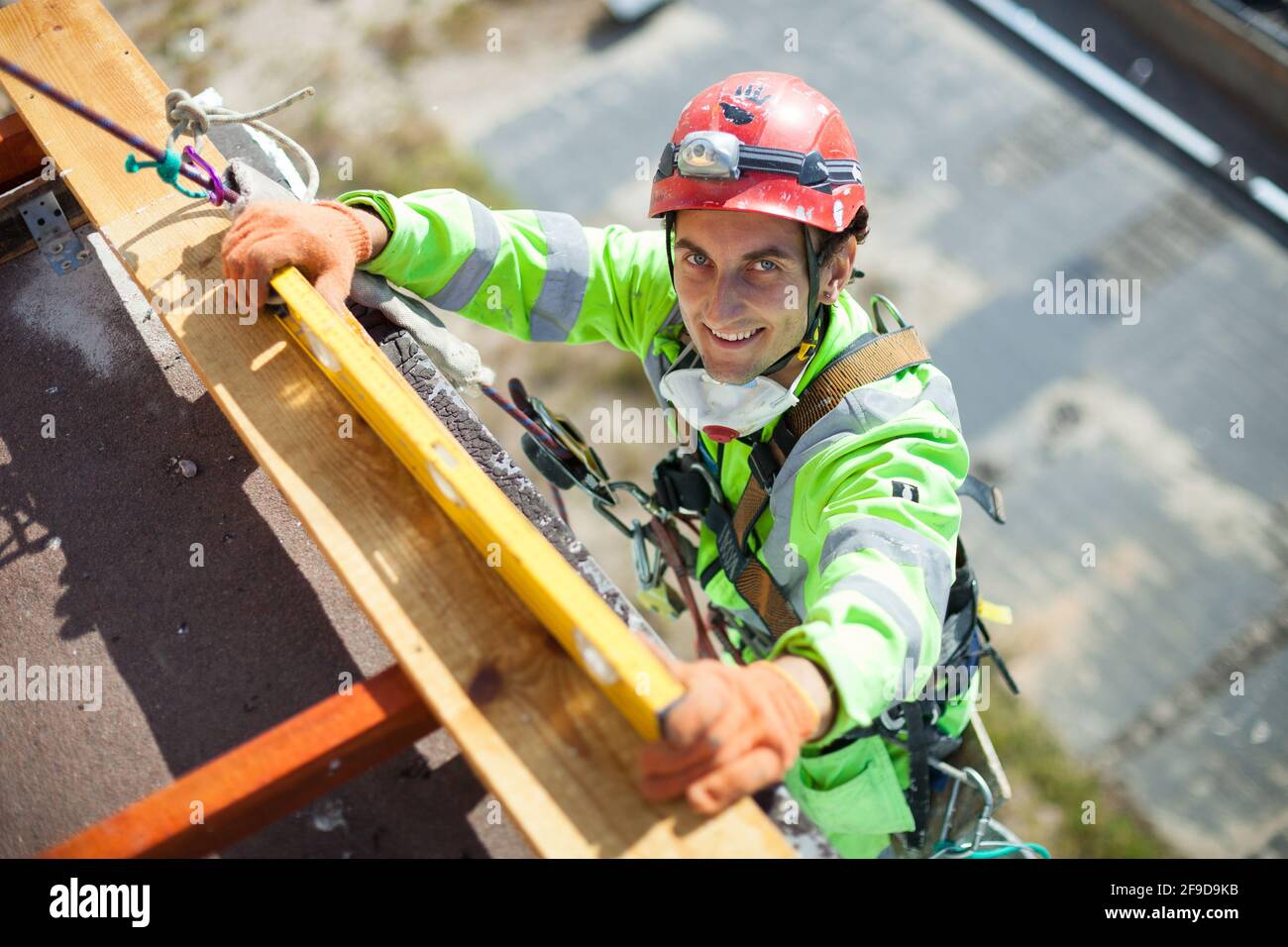 Grimpeur industriel mesurant avec un tube de niveau pendant les travaux de construction, regardant la caméra et souriant Banque D'Images