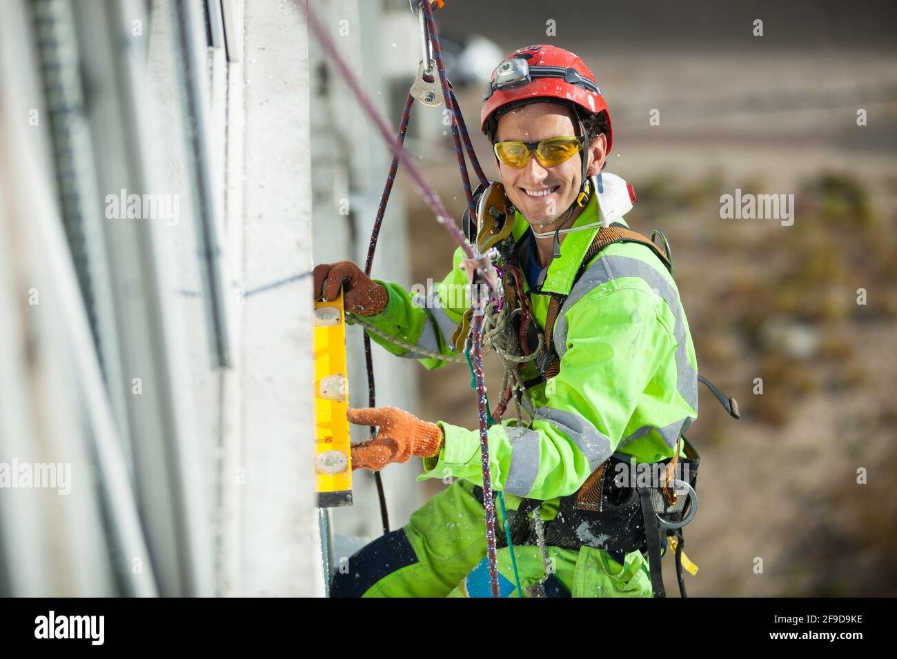 Grimpeur industriel gai mesurant avec un tube de niveau pendant les travaux de construction Banque D'Images