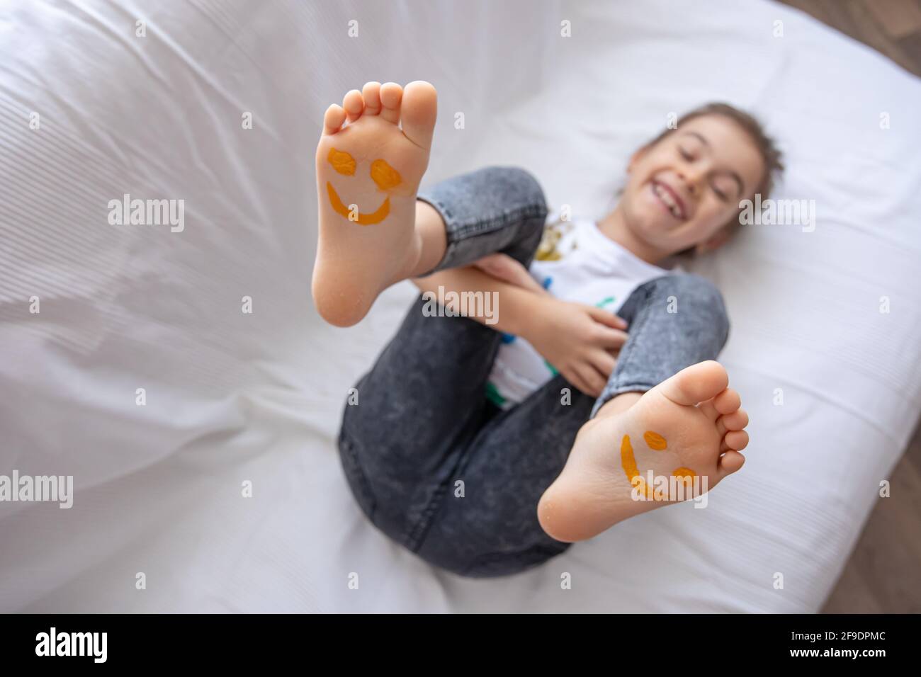 Une petite fille est couché sur un canapé avec ses pieds peints avec des peintures. Sourires amusants sur les pieds des enfants. Banque D'Images