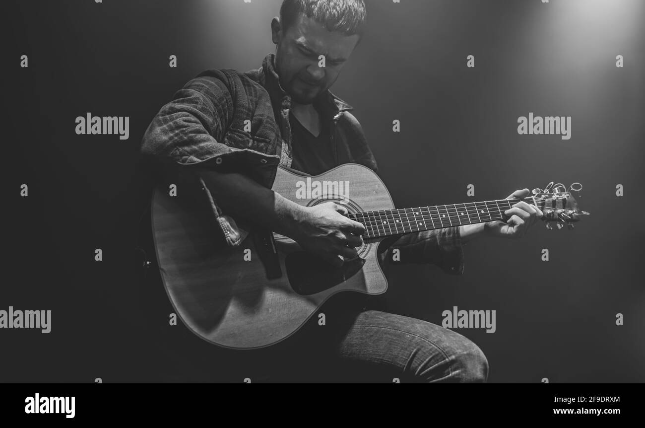 Un homme joue une guitare acoustique à un concert partiellement éclairé. Banque D'Images