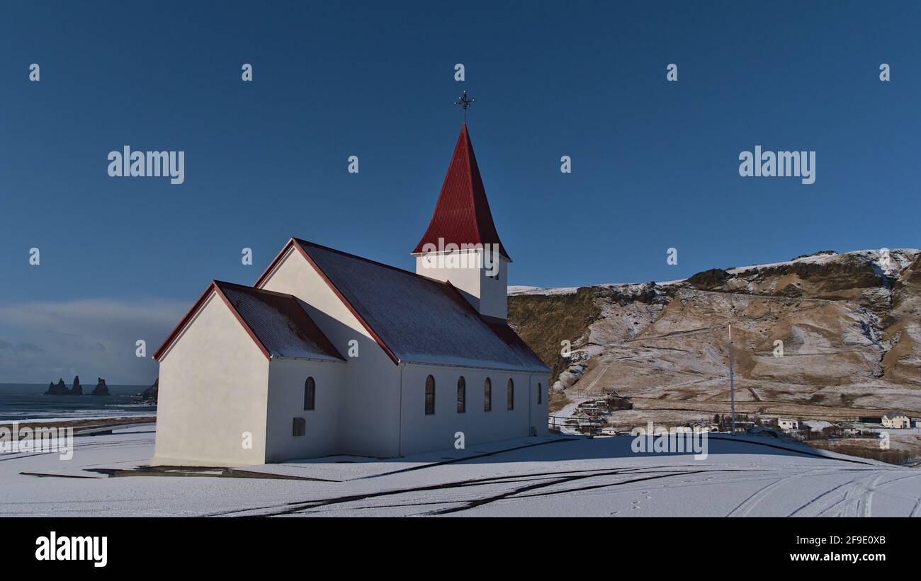 Belle vue sur la petite église située au-dessus du village de Vík í Mýrdal sur la côte sud de l'Islande avec l'océan atlantique et Reynisdrangar formation de roche. Banque D'Images