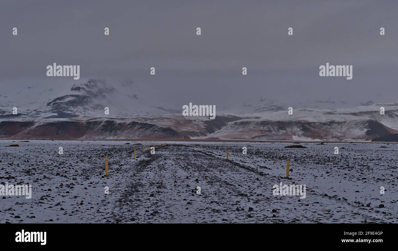 Paysage stérile avec sentier de randonnée jusqu'à l'épave de l'avion DC-3 à Sólheimasandur sur la côte sud de l'Islande avec des montagnes enneigées. Banque D'Images