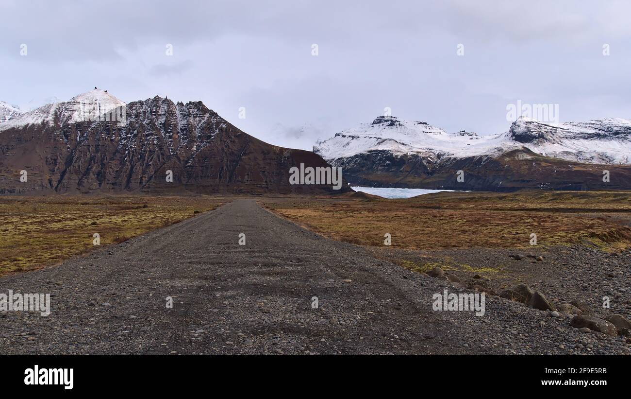Paysage accidenté avec une perspective décroissante de route de gravier menant au glacier Svínafellsjökull dans la chaîne de montagne de Öræfajökull dans le sud de l'Islande. Banque D'Images
