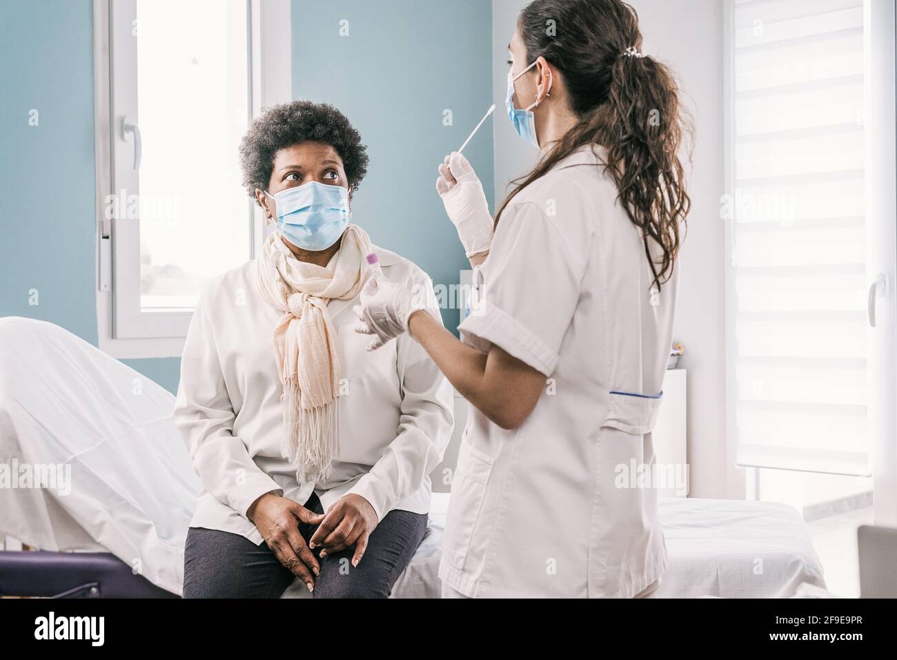 Femme médecin spécialiste en uniforme de protection, gants en latex et masque facial faisant le test nasal du coronavirus sur la femme africaine américaine mature patient dans c Banque D'Images