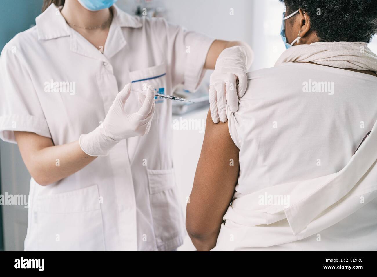 Écourtée non reconnaissable femme médecin spécialiste en uniforme de protection, gants en latex et masque facial vaccinant anonyme africaine américaine mature femme Banque D'Images
