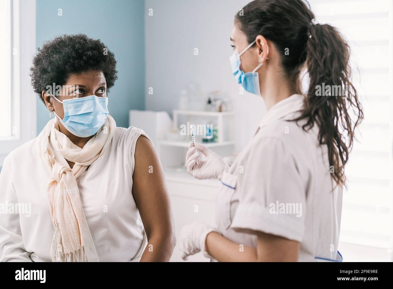 Femme médecin spécialiste en uniforme de protection, gants en latex et masque facial vaccinant la patiente africaine américaine mature en clinique pendant le coronav Banque D'Images