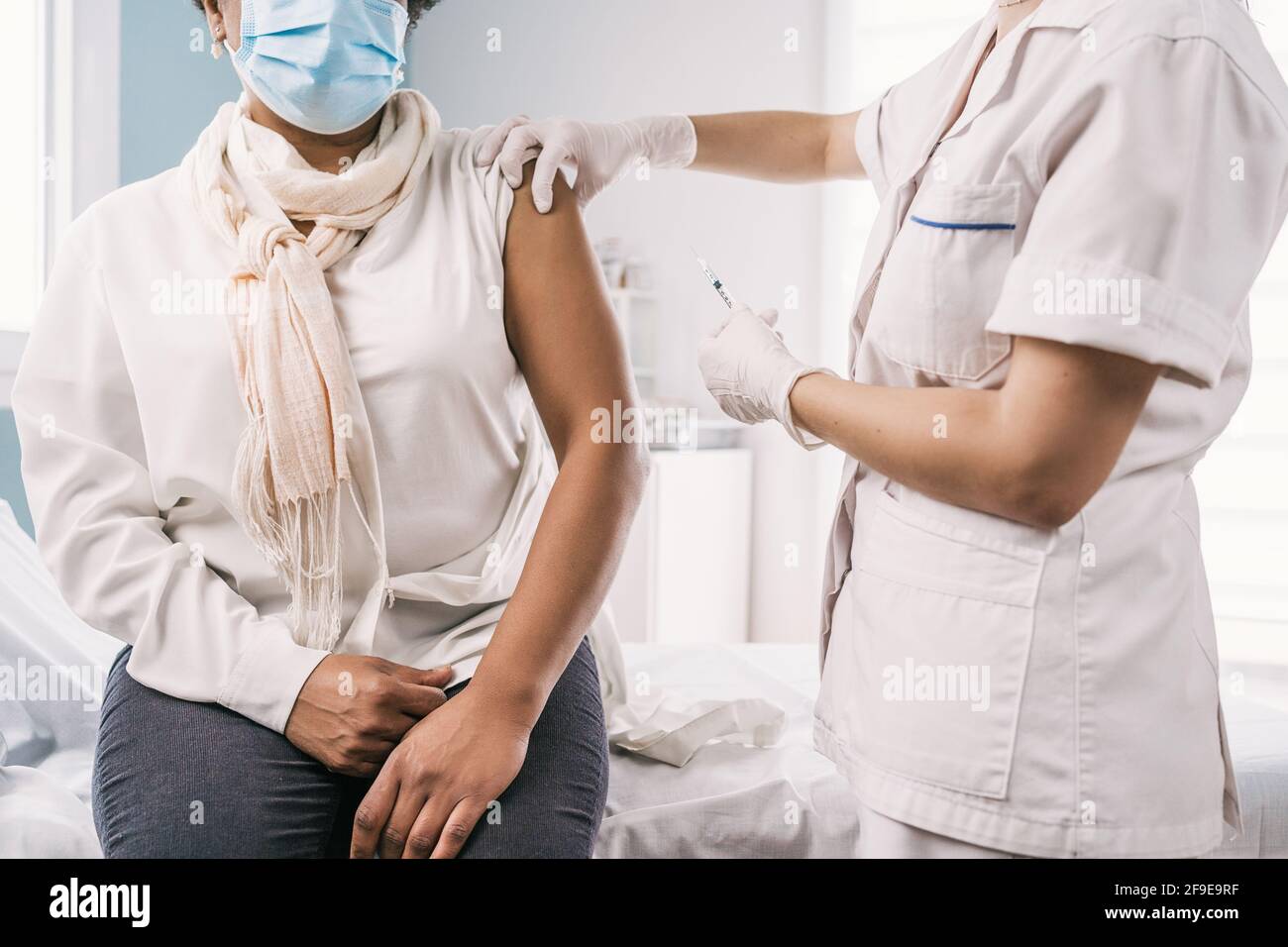 Écourtée non reconnaissable femme médecin spécialiste en uniforme de protection, gants en latex et masque facial vaccinant anonyme africaine américaine mature femme Banque D'Images