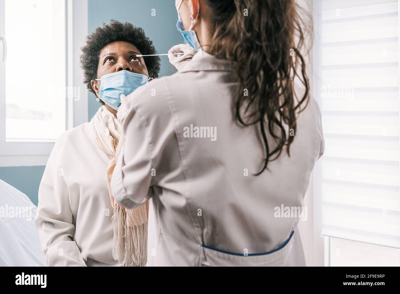 Femme médecin spécialiste en uniforme de protection, gants en latex et masque facial faisant le test nasal du coronavirus sur la femme africaine américaine mature patient dans c Banque D'Images