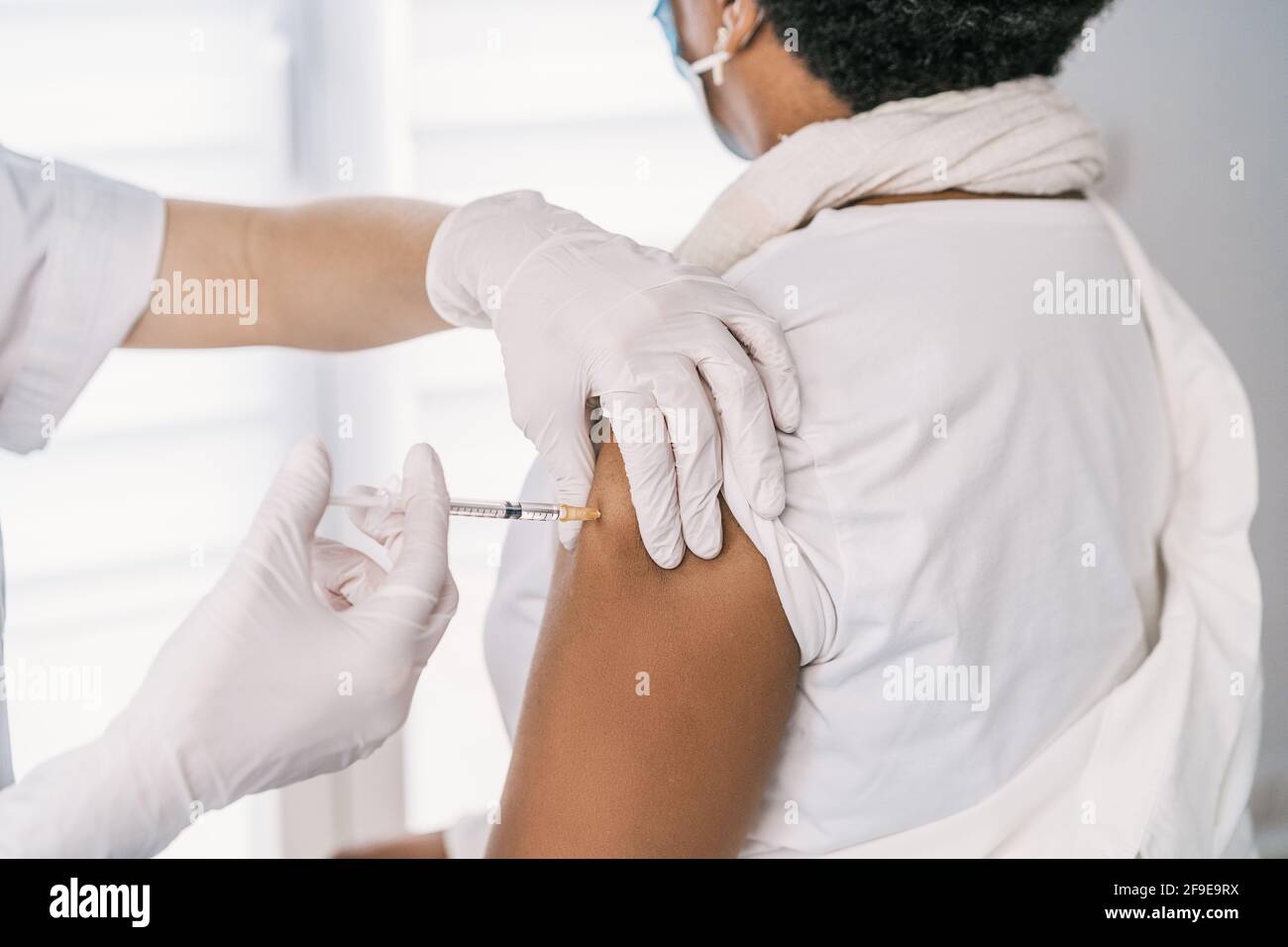 Écourtée non reconnaissable femme médecin spécialiste en uniforme de protection, gants en latex et masque facial vaccinant anonyme africaine américaine mature femme Banque D'Images