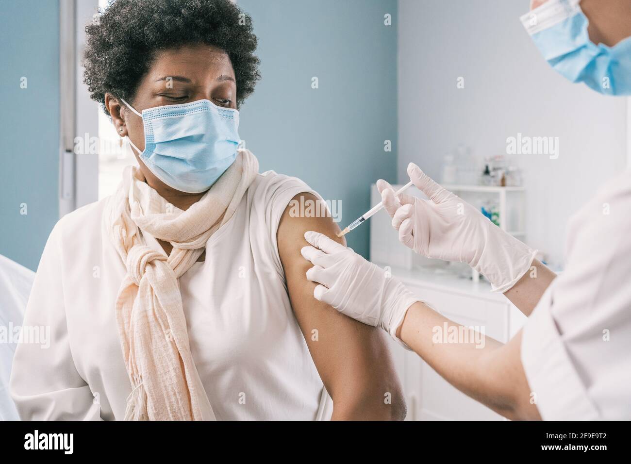 Écourtée non reconnaissable femme médecin spécialiste en uniforme de protection, gants en latex et masque facial vaccinant la femme africaine américaine mature patient i Banque D'Images